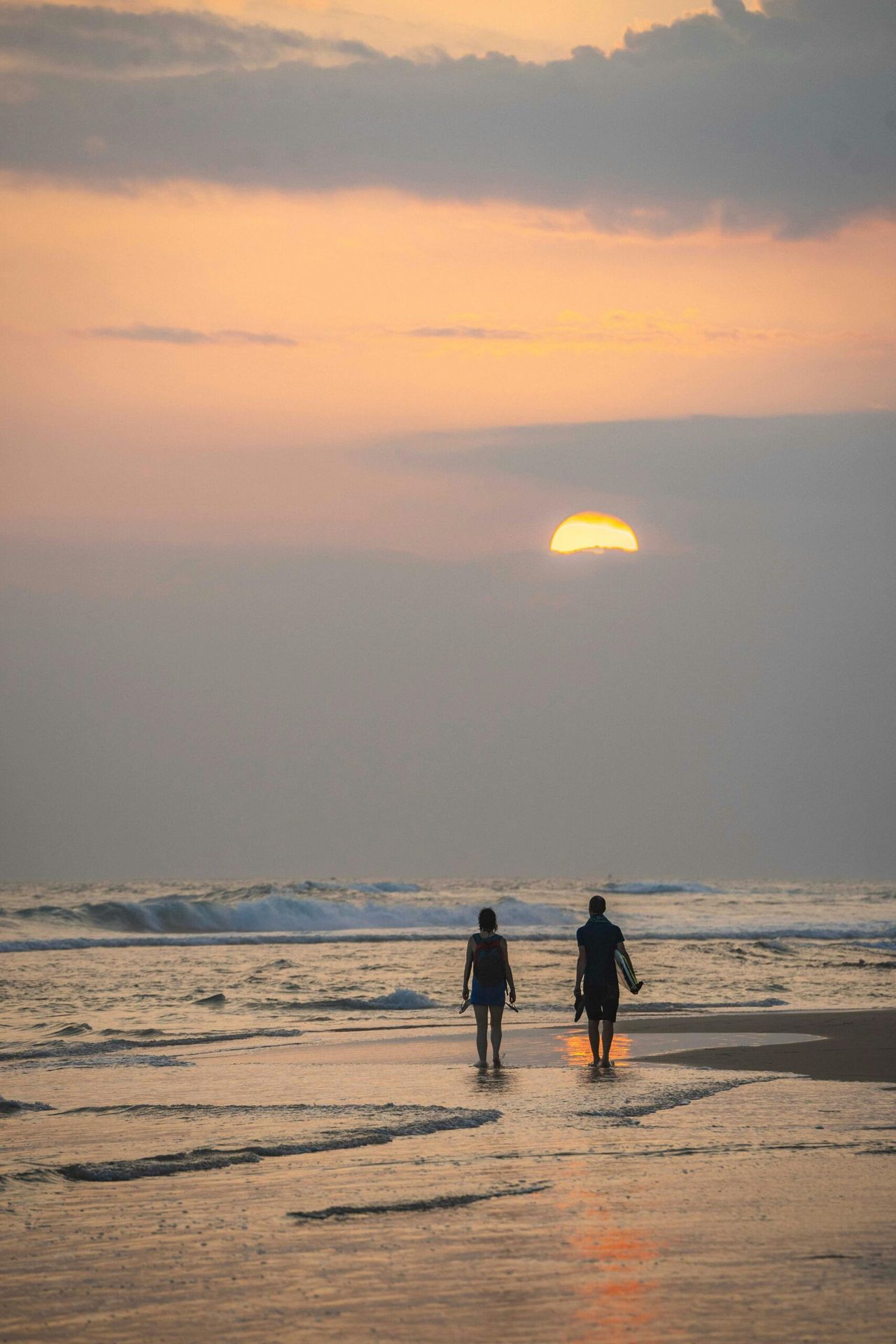 Two people walking on the beach at sunset